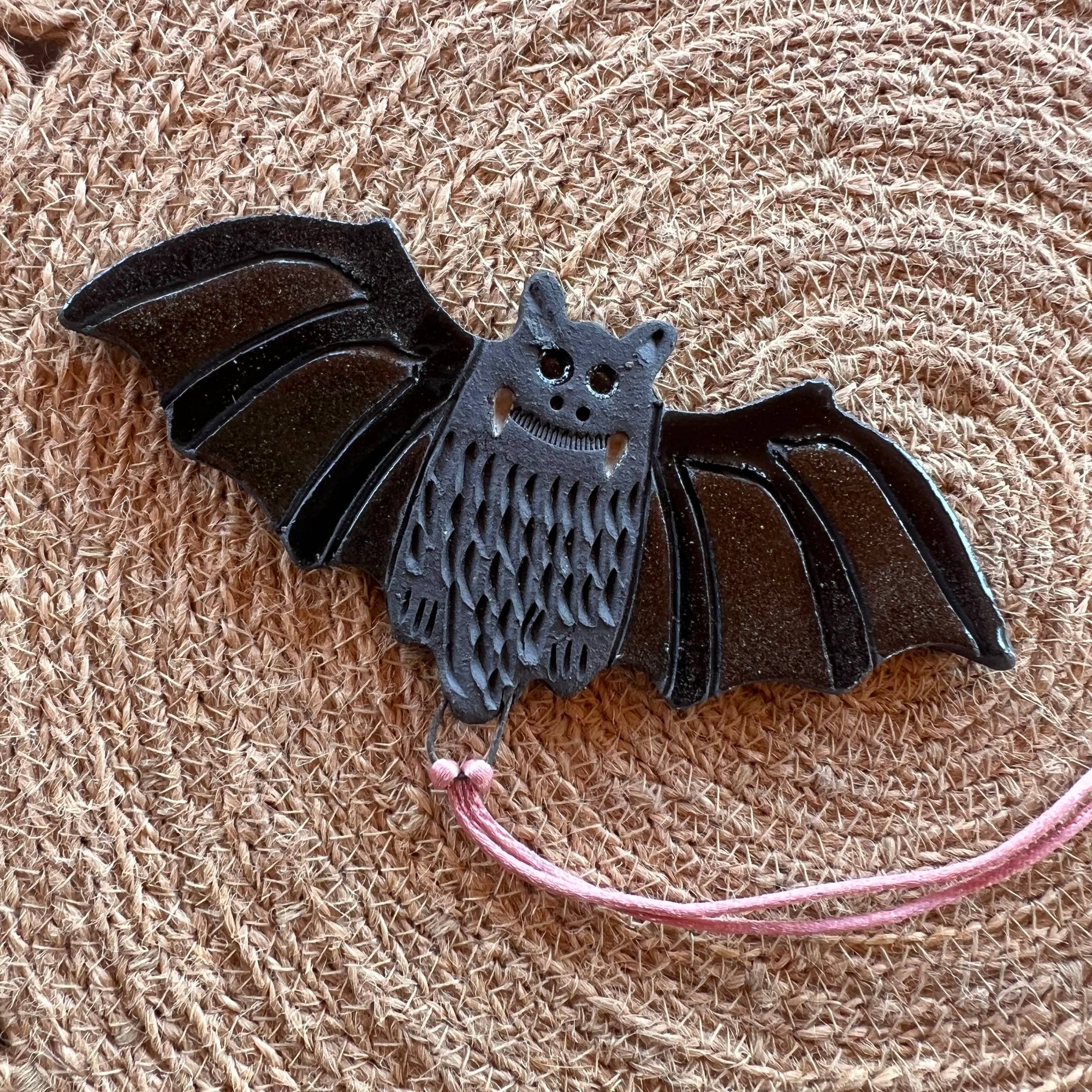 Bat-shaped ornament with a pink thread on a textured beige background