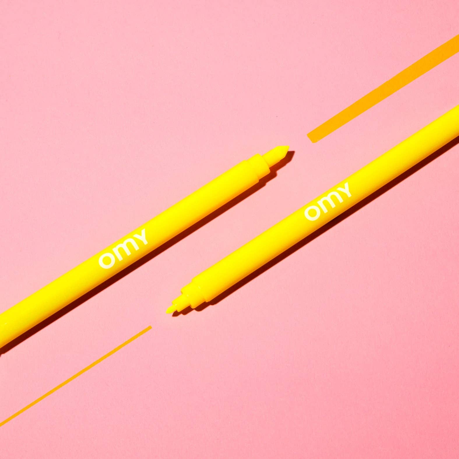 Two yellow markers with 'omy' branding on a pink background