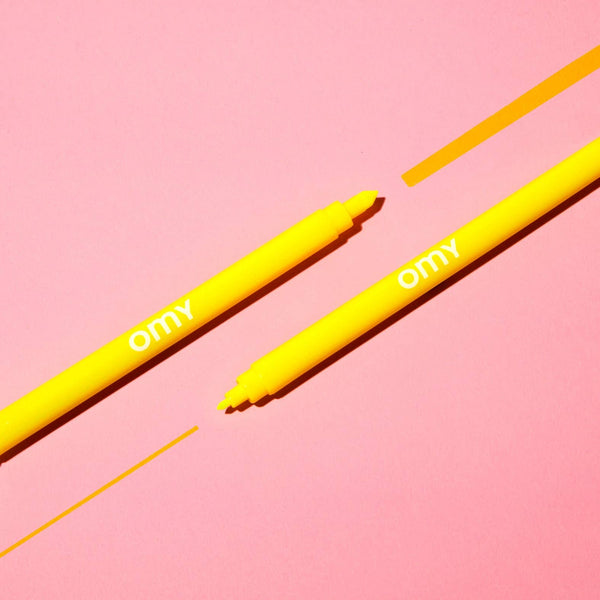 Two yellow markers with 'omy' branding on a pink background