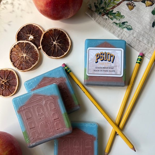 Three bars of soap with a house design, a pencil, an apple, and dried oranges on a white surface.