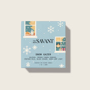 Candle packaging for 'Snow Gazer' by The New Savant on a light blue background with snowflake designs.