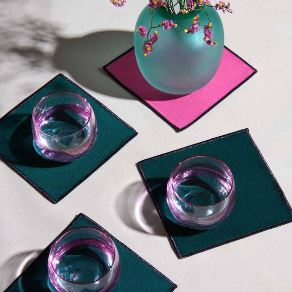 Two glasses on green coasters with a teal vase with flowers on a pink coaster.