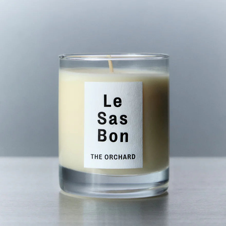 Candle with 'Le Sas Bon' label on a reflective surface and gray background