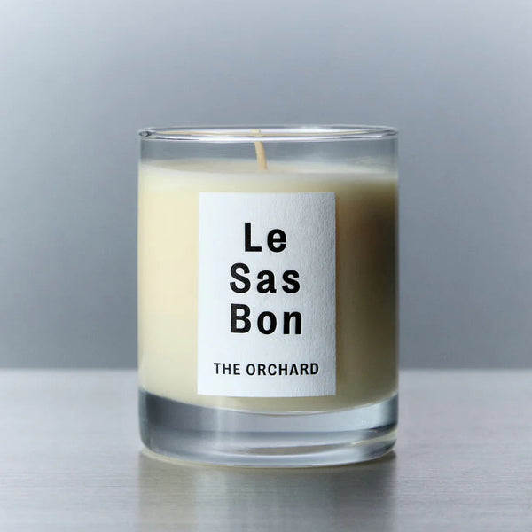 Candle with 'Le Sas Bon' label on a reflective surface and gray background