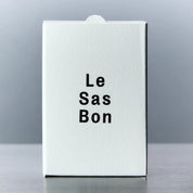White box with 'Le Sas Bon' text on a reflective surface and gray background