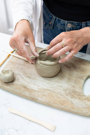 Person shaping clay on a wooden board with tools