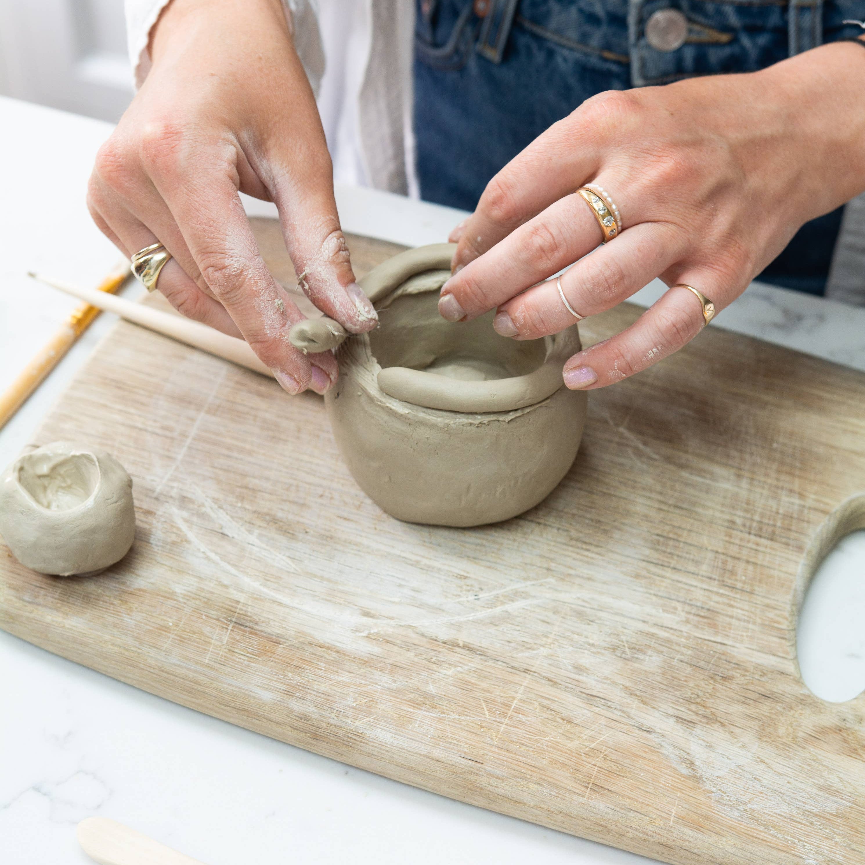 Person shaping clay on a wooden board with tools