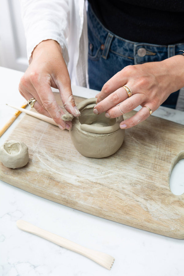 Person shaping clay on a wooden board with tools