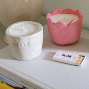 Two candles, one white and one pink, on a surface with a matchbox labeled 'Sculpt'.