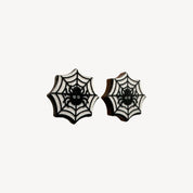 A pair of black and white spiderweb stud earrings with a small spider design in the center, shown on a plain off-white background.