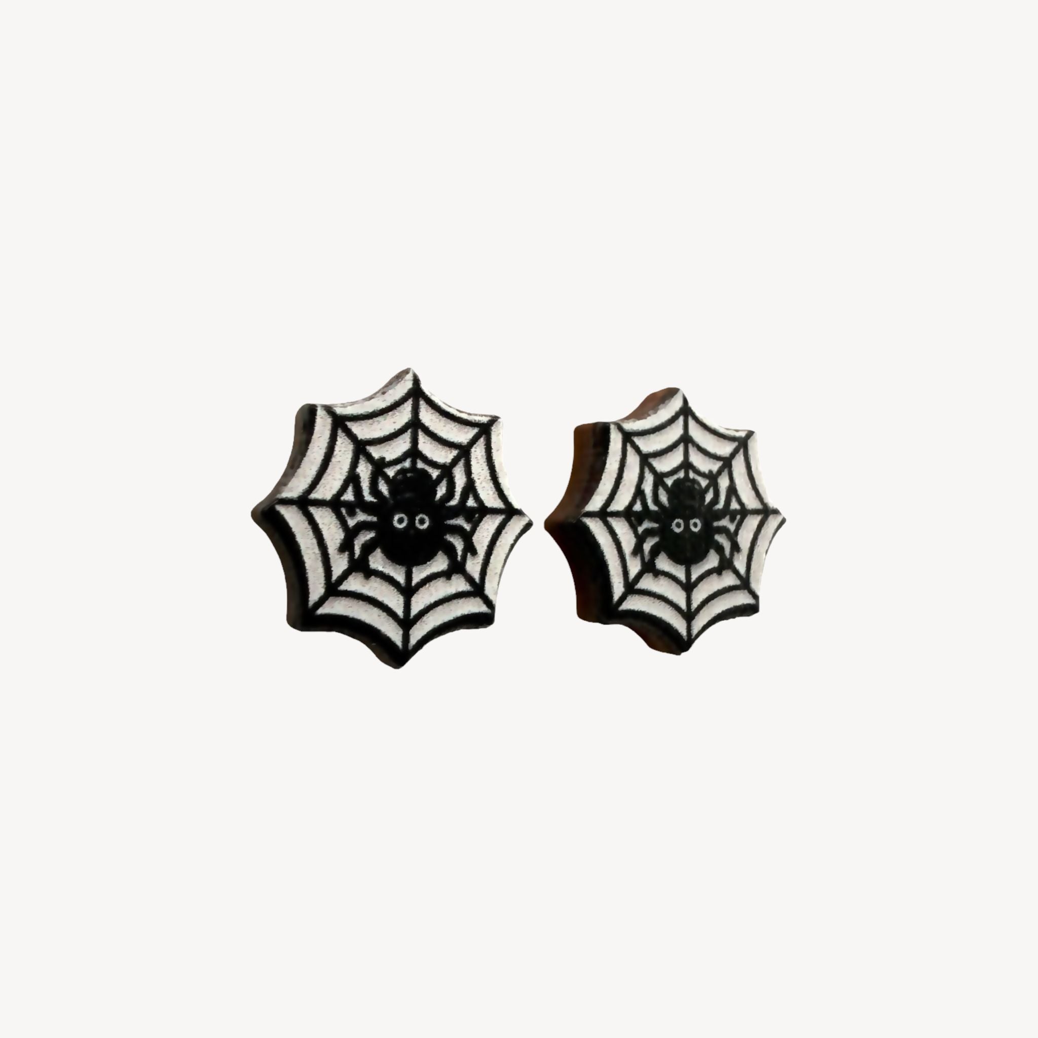 A pair of black and white spiderweb stud earrings with a small spider design in the center, shown on a plain off-white background.