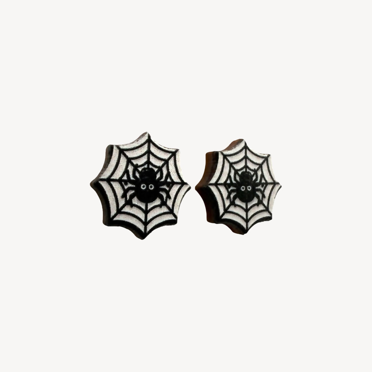 A pair of black and white spiderweb stud earrings with a small spider design in the center, shown on a plain off-white background.
