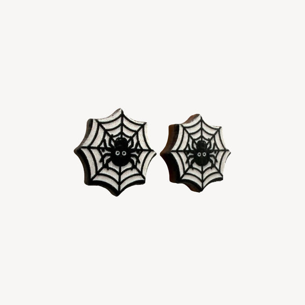 A pair of black and white spiderweb stud earrings with a small spider design in the center, shown on a plain off-white background.