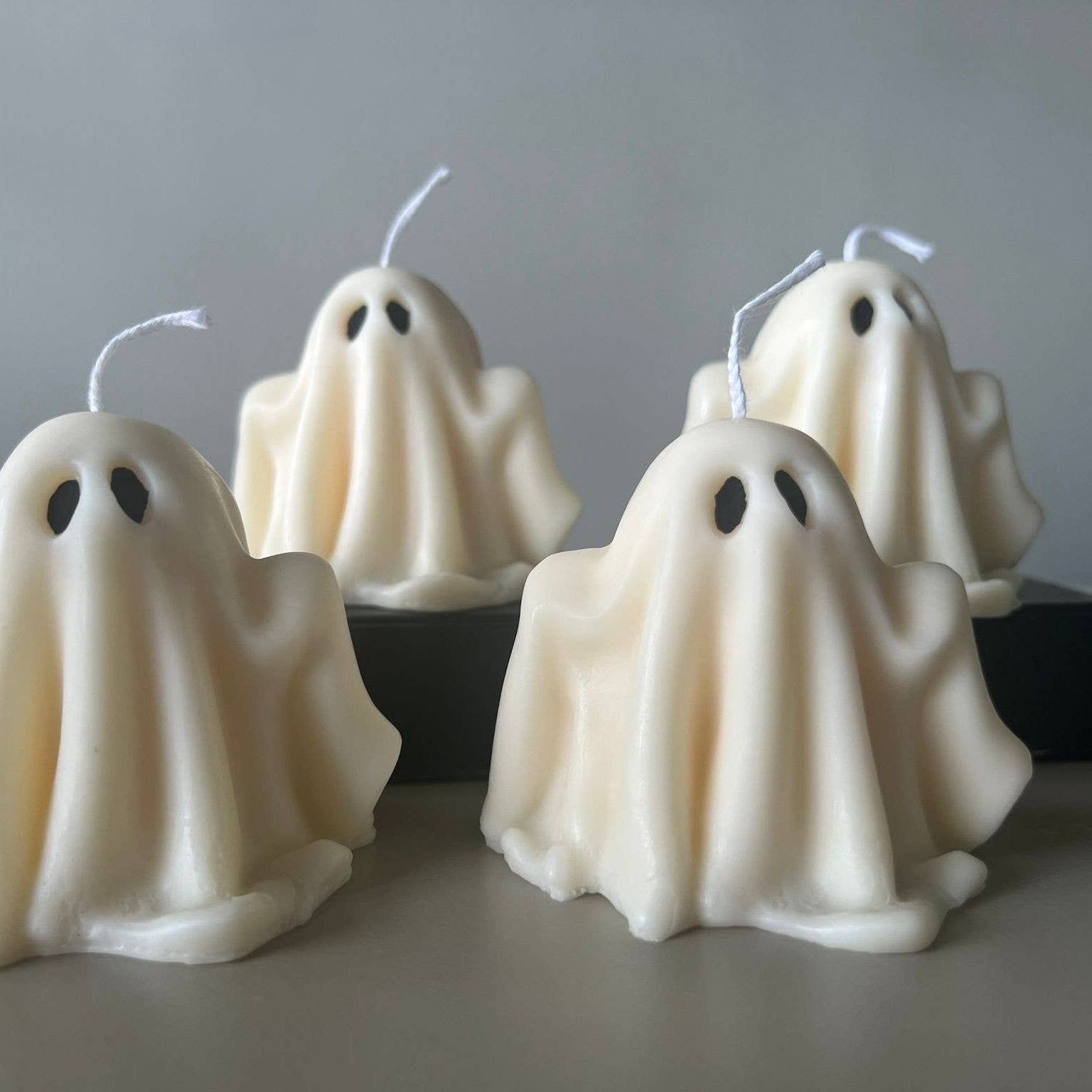 Four ghost-shaped candles on a neutral background