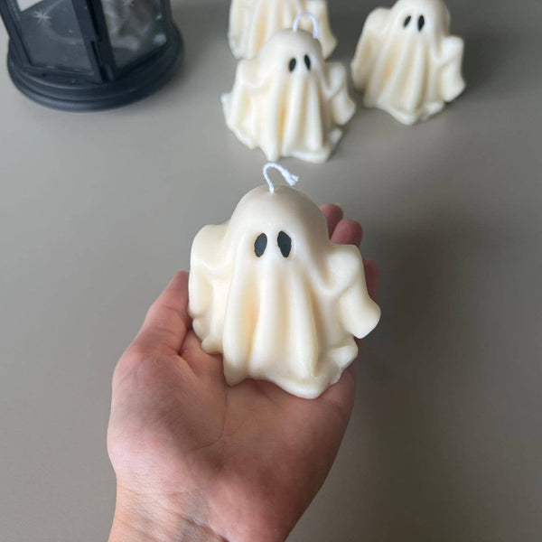 Hand holding a white ghost-shaped candle with more ghost candles in the background.