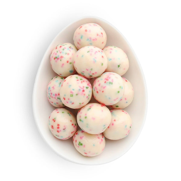 White bowl filled with round, white candies with colorful sprinkles on a white background