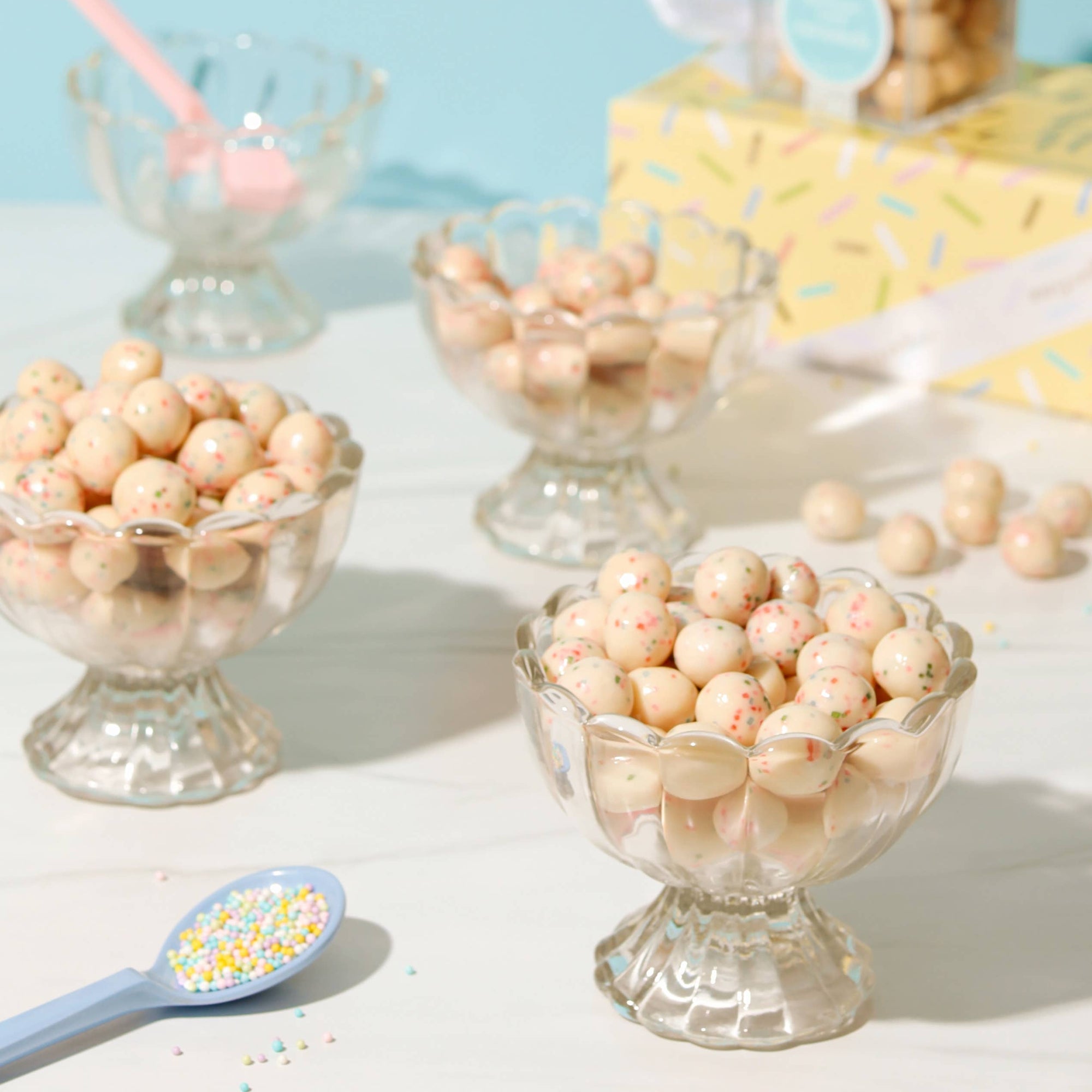 Decorative bowls filled with small round candies on a light surface with a blue background.