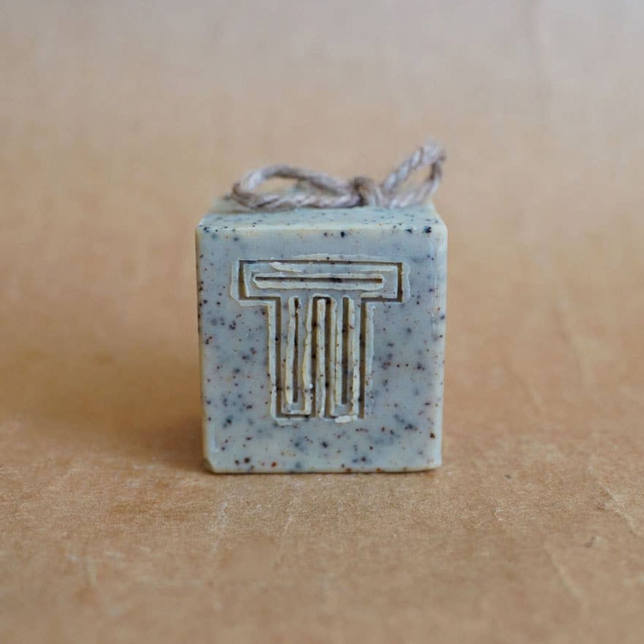 A square bar of soap with two letter T's carved into it, with a natural string on top.