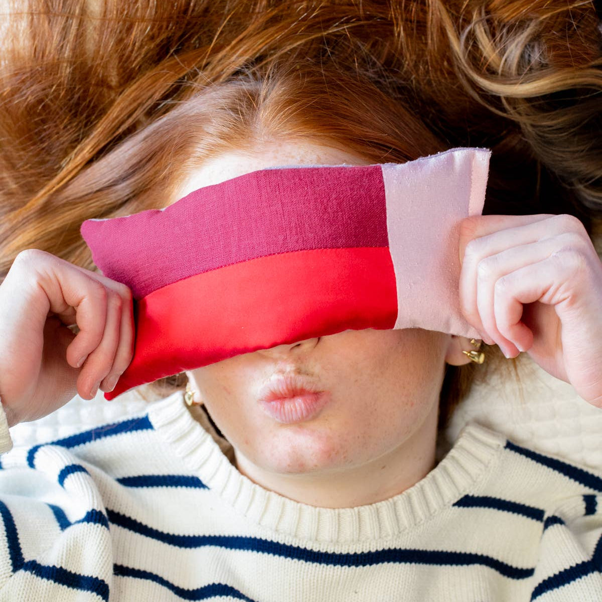 Person wearing a striped sweater with a colorful eye pillow over their eyes.