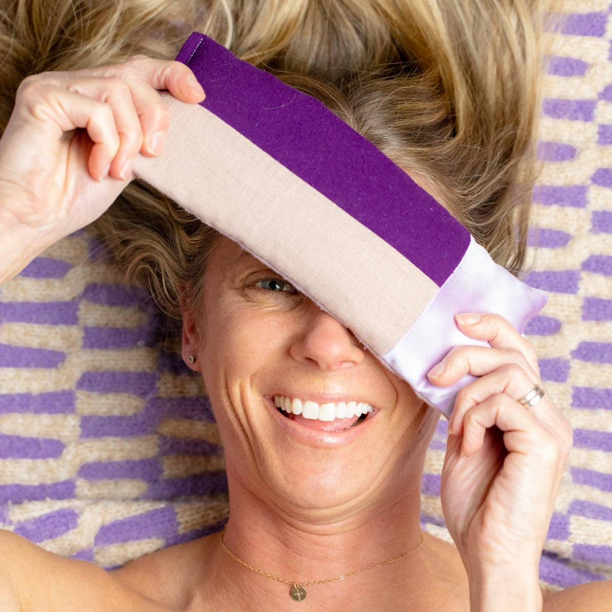 Woman holding a purple eye pillow with a striped towel in the background