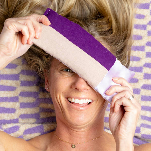 Woman holding a purple eye pillow with a striped towel in the background