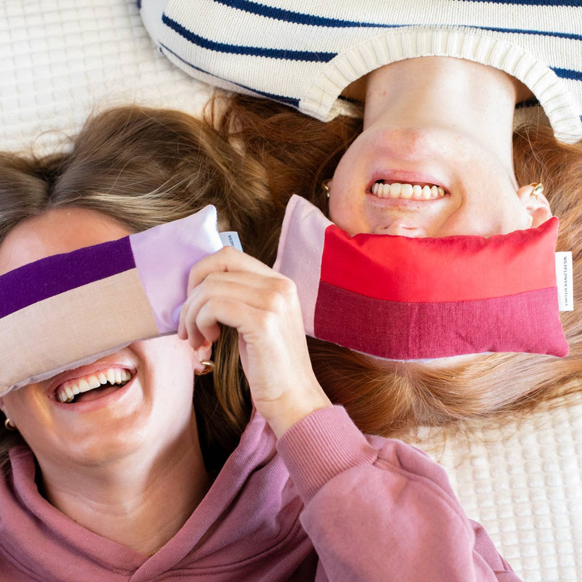 Two people wearing colorful eye masks on a light background