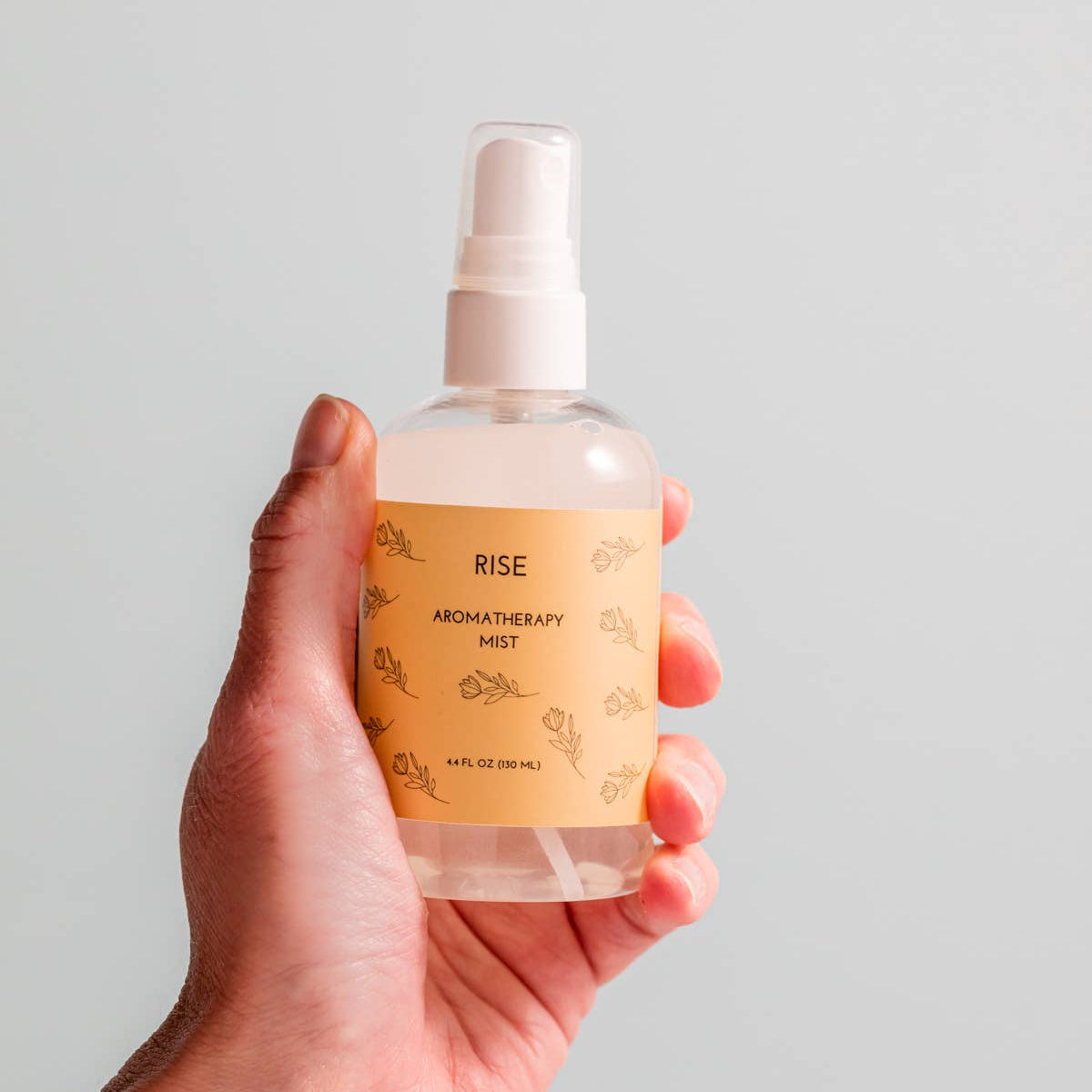 Hand holding a bottle of 'Rise' aromatherapy mist against a plain background