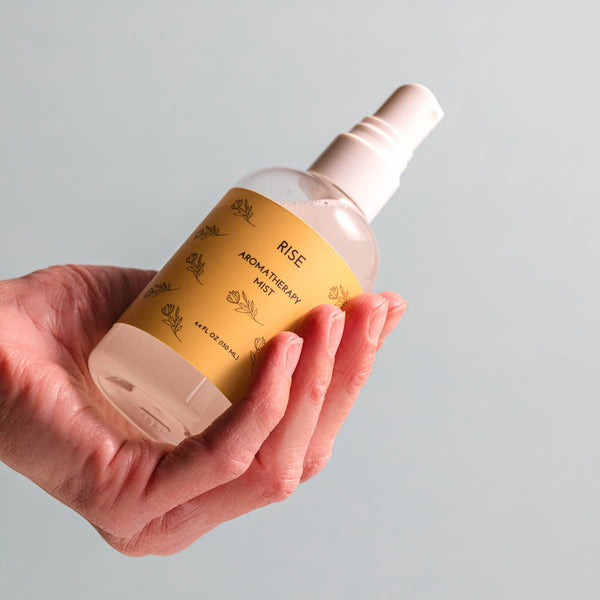 Hand holding a bottle of 'RISE' product against a plain background
