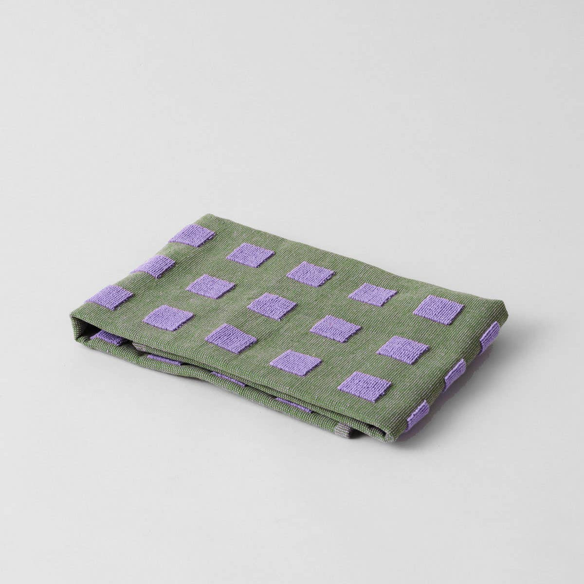 Folded green fabric with purple square patterns on a light gray background
