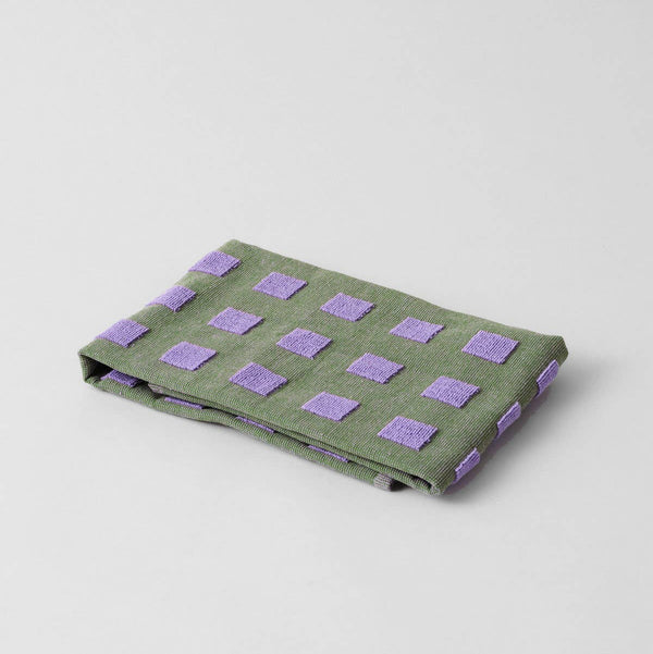 Folded green fabric with purple square patterns on a light gray background