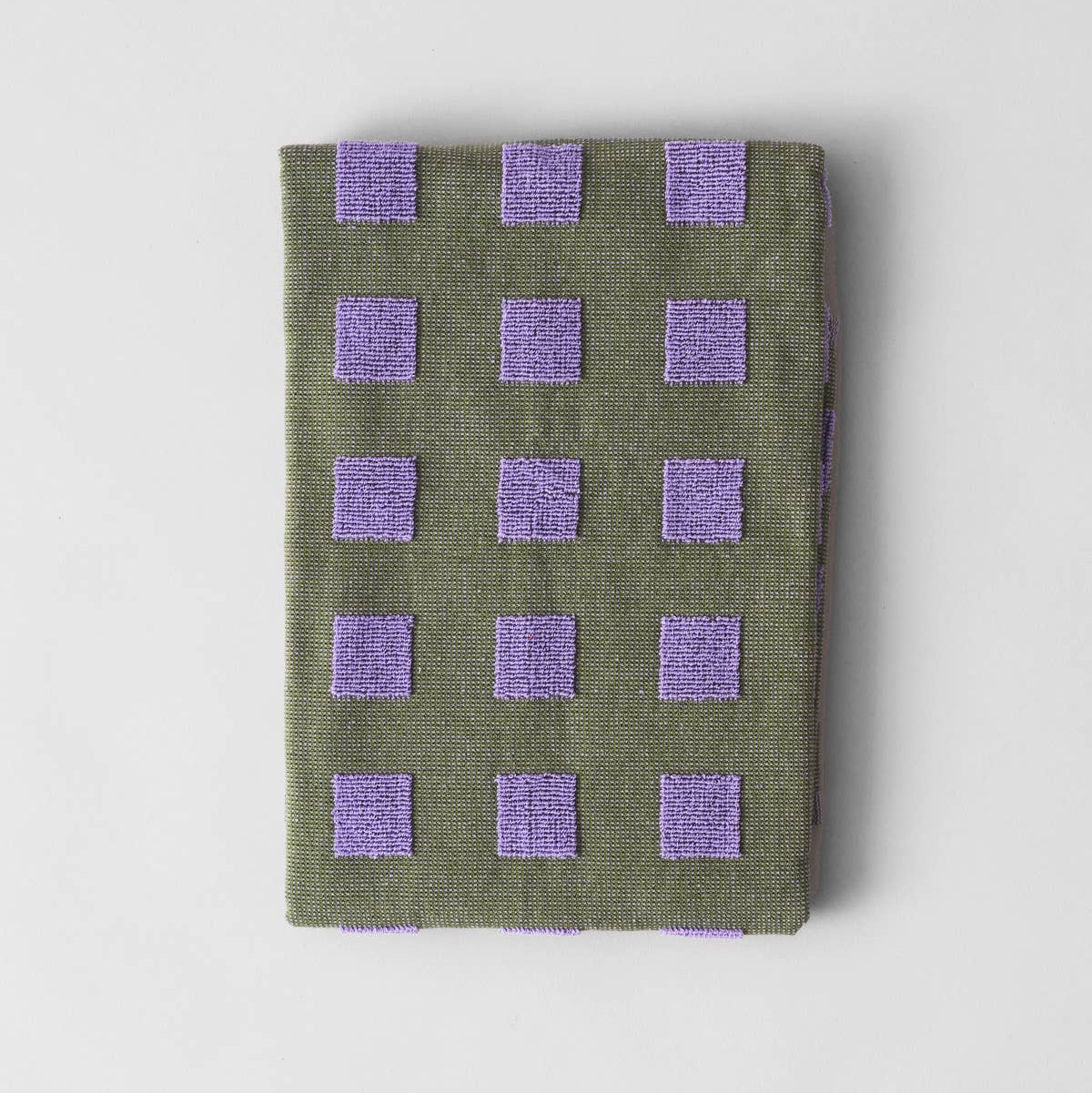 Folded green fabric with purple square patterns on a light gray background