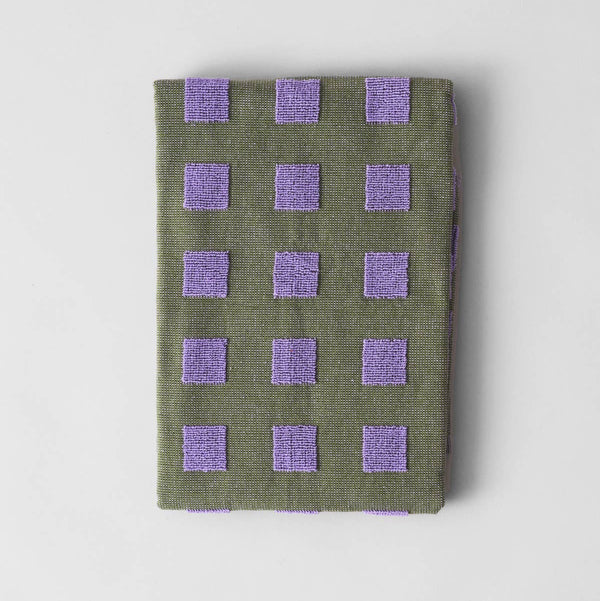 Folded green fabric with purple square patterns on a light gray background