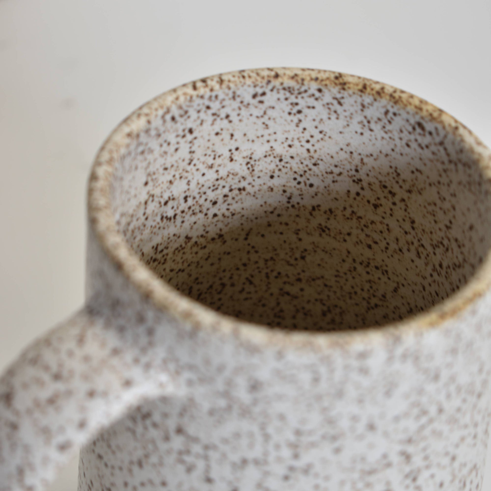 Detail of a cream speckled ceramic mug on a light background