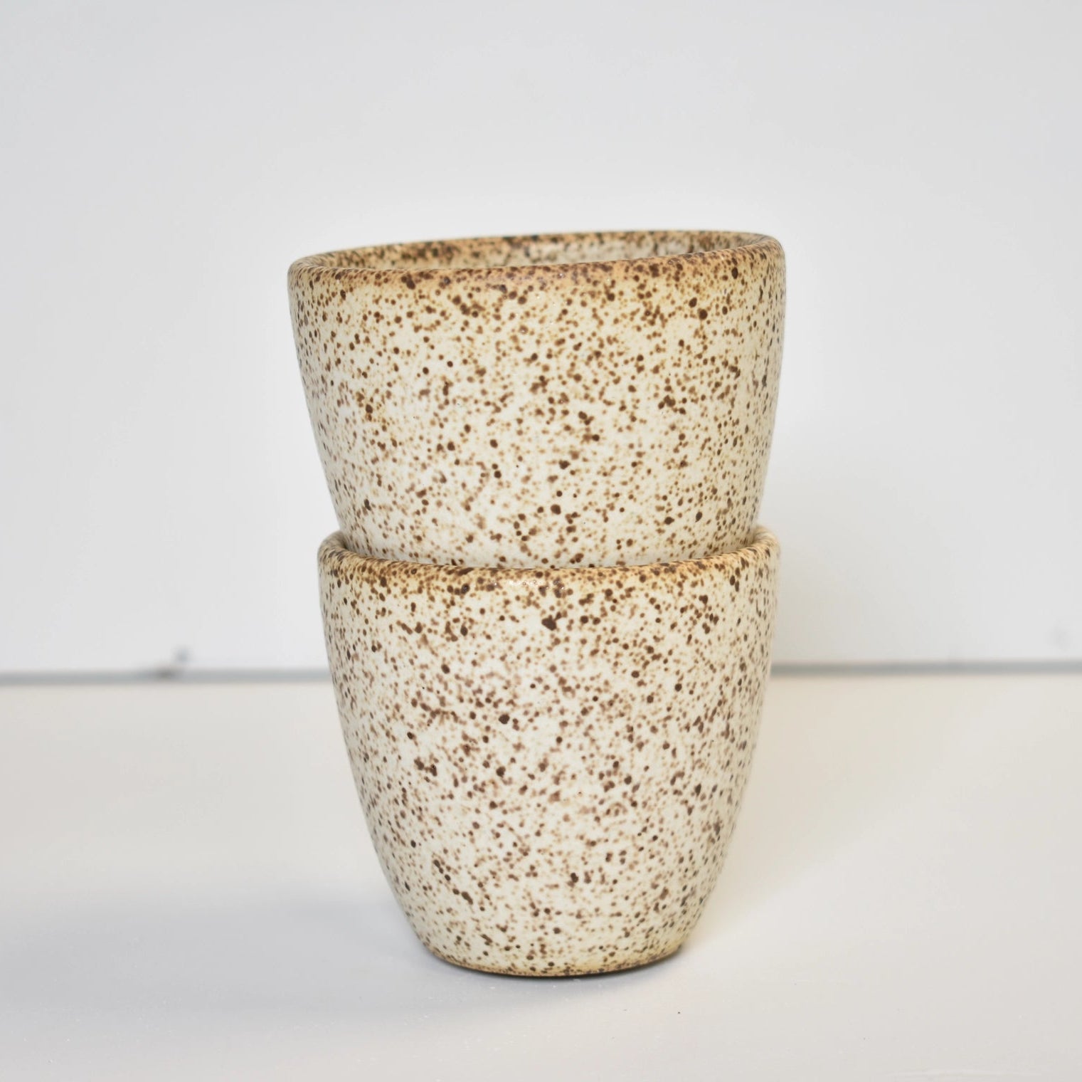 Two stacked ceramic cups with a speckled pattern on a white background